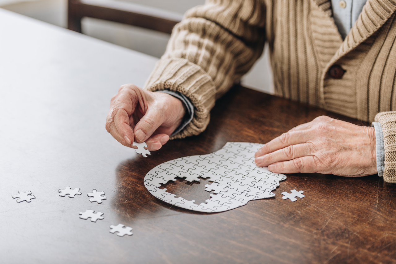 Hands of an older person assemble a jigsaw puzzle shaped like a human head in profile