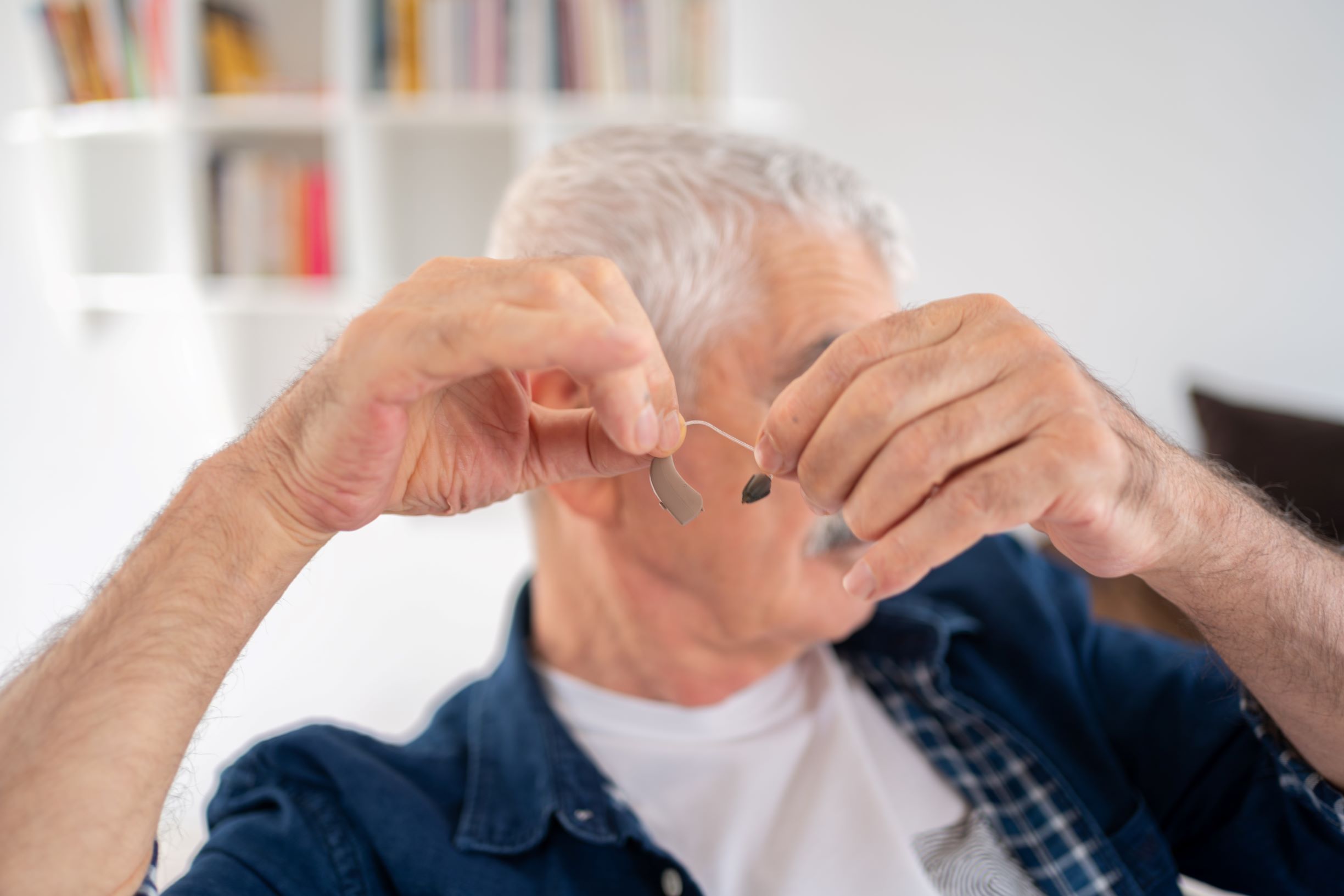 A man with gray hair holds a delicate hearing aid between his two hands 