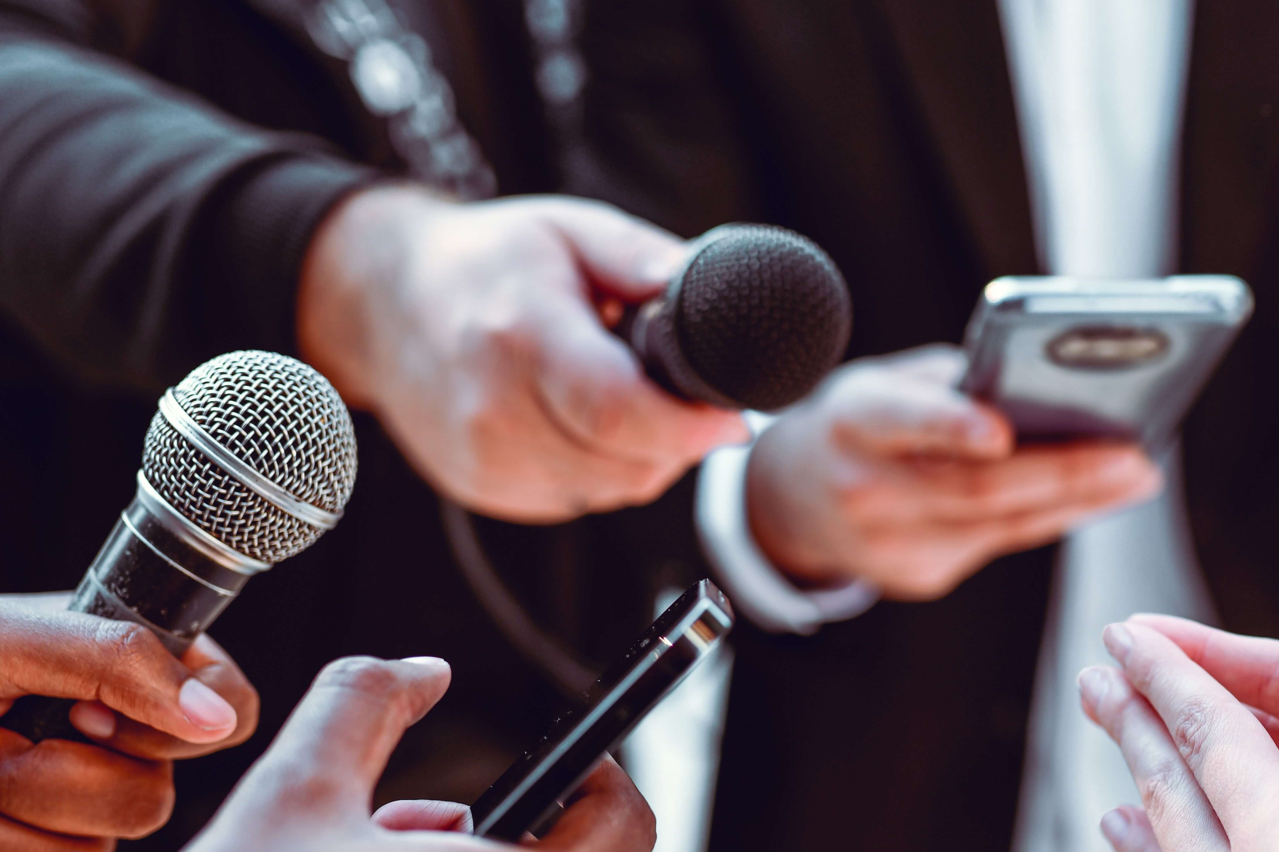 multiple handheld microphones are pointed toward a white coated person being interviewed