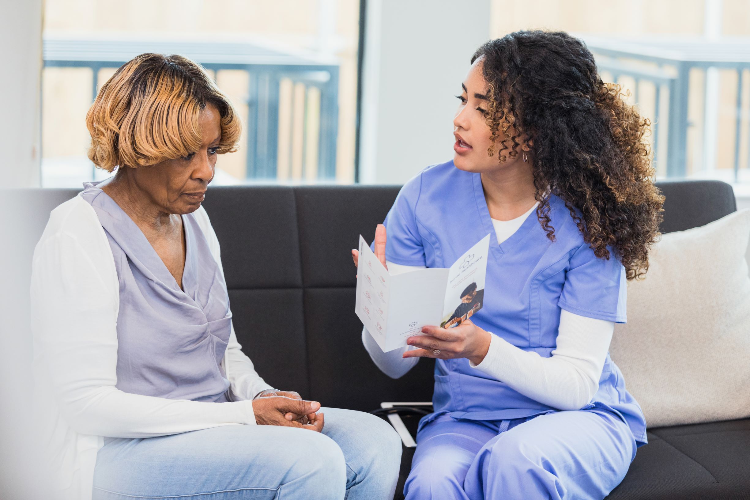 A scrub-clad healthcare worker shows an older woman a brochure