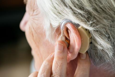 an older person touches the hearing aid in their left ear